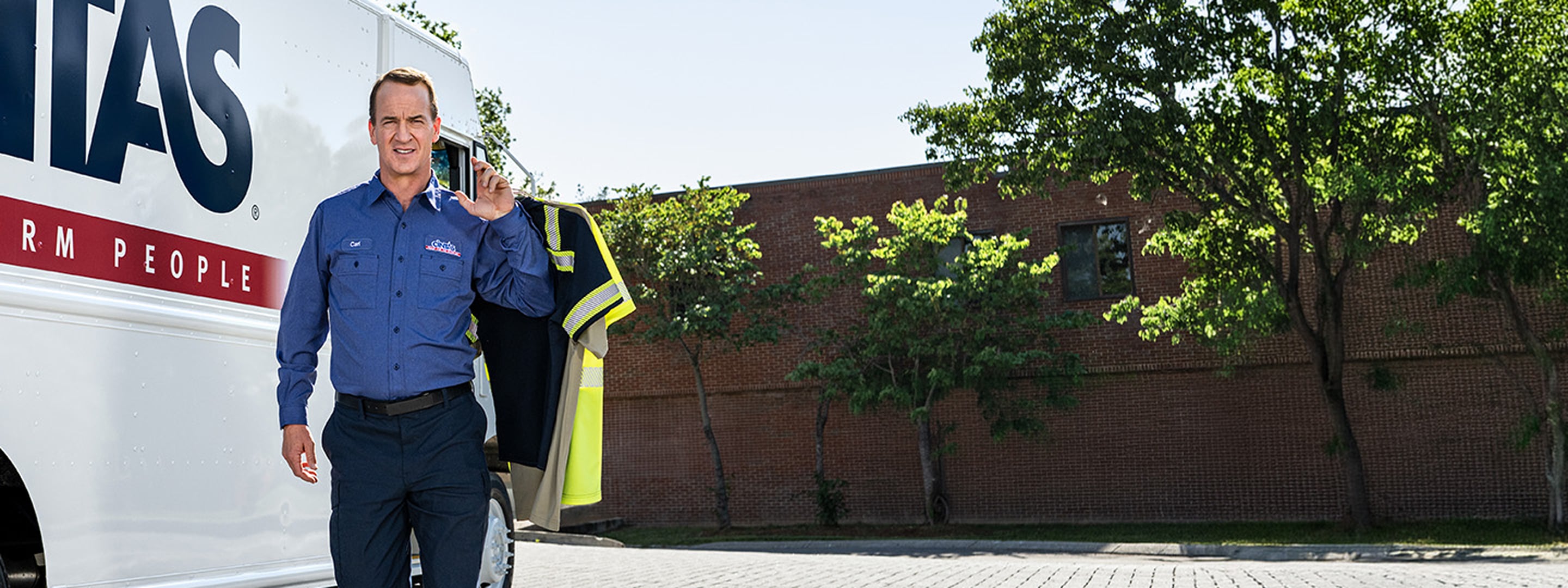 cintas service representative carrying workwear shirts in front of a cintas truck