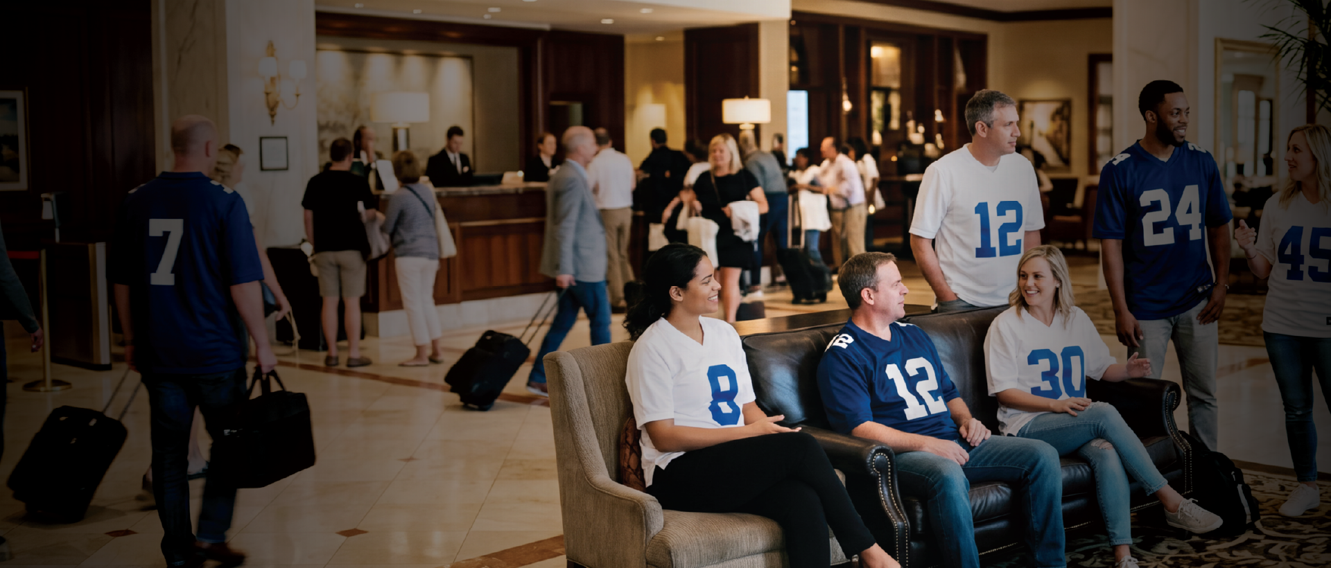 Attendees in numbered sports jerseys gather and socialize in a busy hotel lobby.